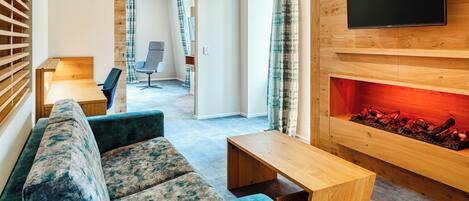Een moderne woonkamer met een bank, een salontafel, een open haard en een televisie bevestigd aan een houten wand.