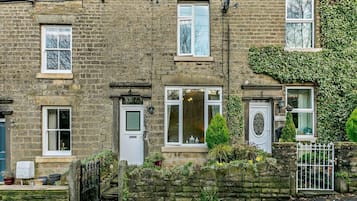 A traditional stone house with multiple windows, a front door, and a small garden with potted plants.
