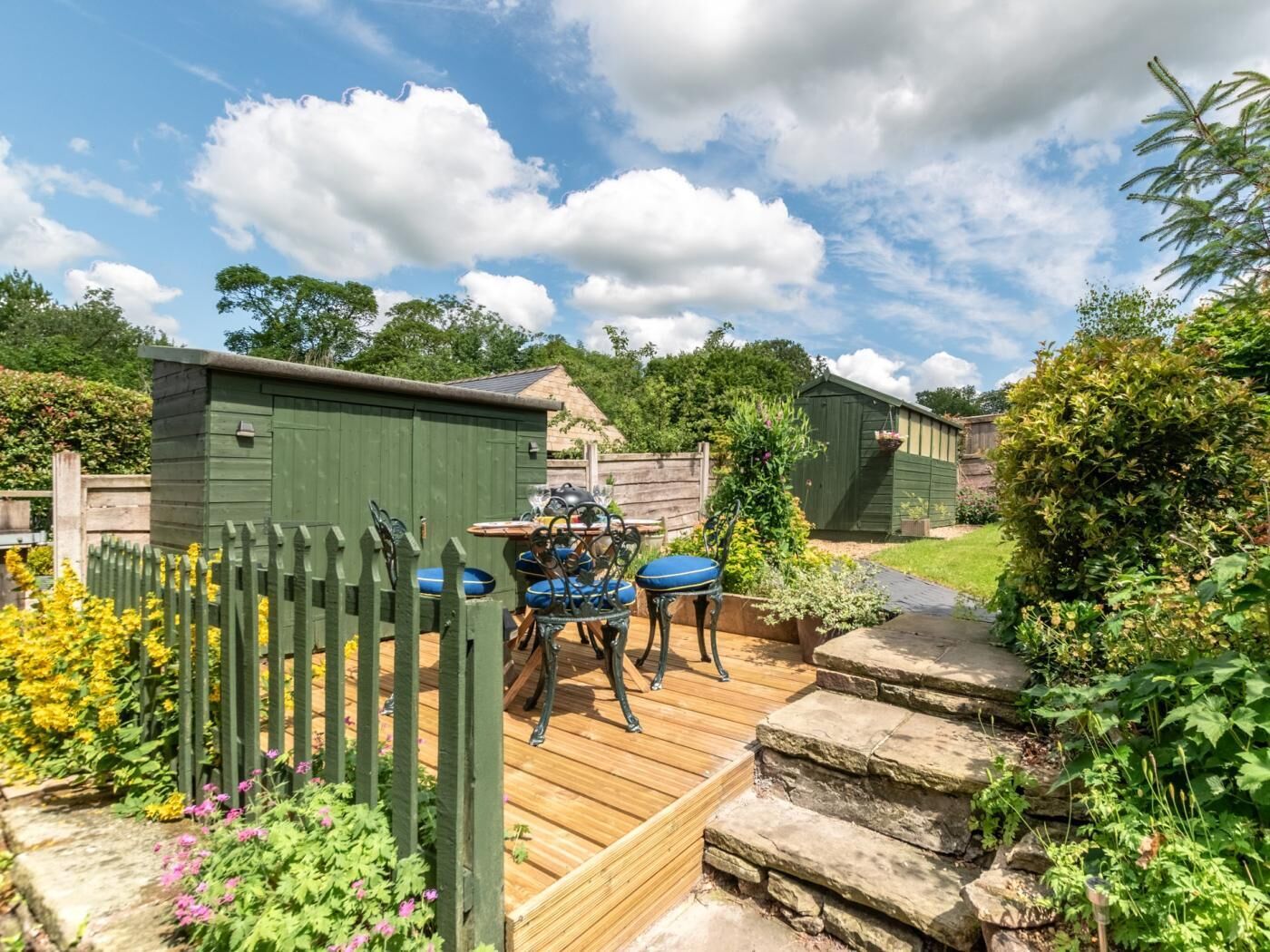 A wooden deck with a table and chairs, surrounded by a wooden fence and garden beds.