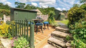 Une terrasse en bois avec une table et des chaises, entourée d’une clôture en bois et de parterres de fleurs.