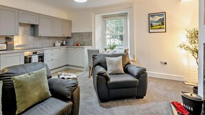 Eine moderne Küche mit grauen Schränken, ein Essbereich mit Tisch und Stühlen sowie ein Wohnzimmer mit zwei Ledersofas.