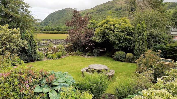 Ein Garten mit Rasen, einem Holztisch und Stühlen sowie verschiedenen Pflanzen.