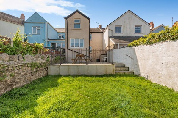 A residential area with houses, a grassy yard, a stone wall, and a wooden bench. - 3 Bed in Tenby (oc-86574) (Tenby)