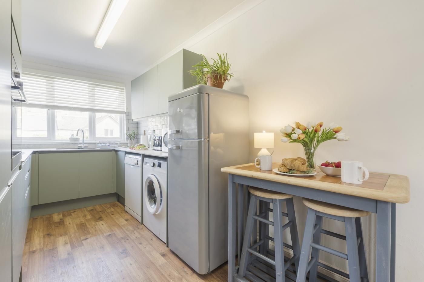 A modern kitchen with a washing machine, a refrigerator, a sink, and a bar area with stools.