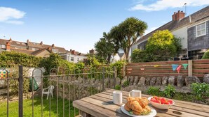 Ein Holztisch mit einem Teller Essen, zwei Tassen und einer Bank in einem Garten.
