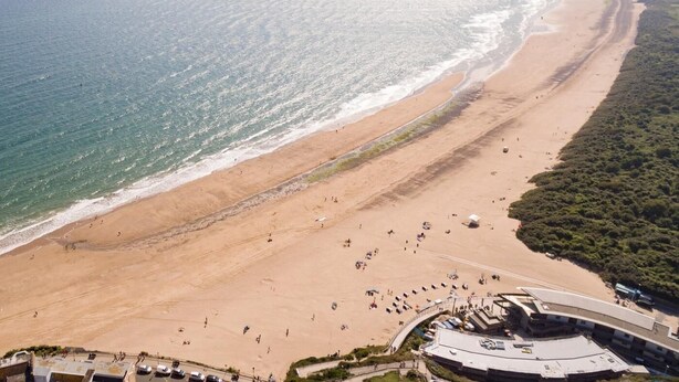 Ein Luftbild einer Bucht mit gewundener Küstenlinie, einem Sandstrand und einigen Personen.
