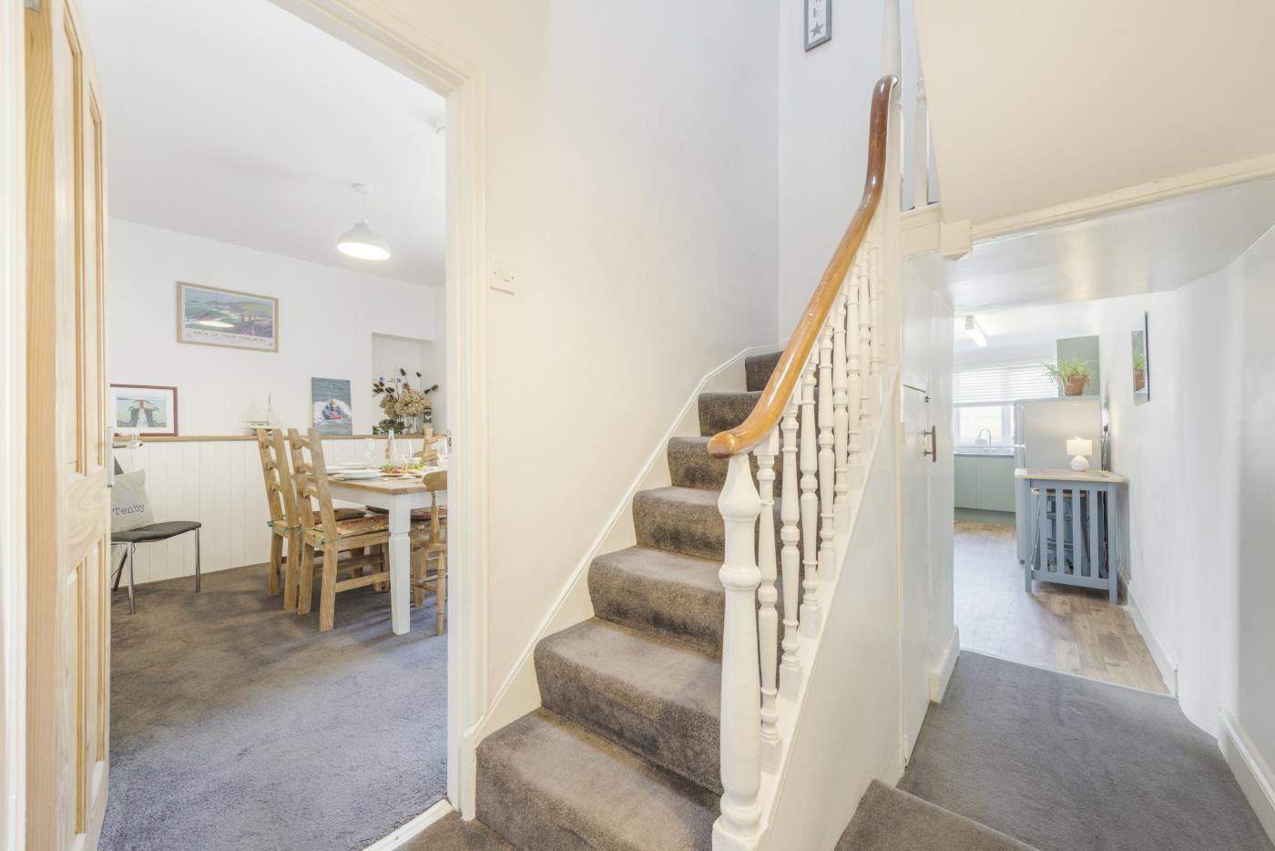 A staircase with a wooden handrail leading to a landing, carpeted floors, and a dining area with wooden chairs and a table.