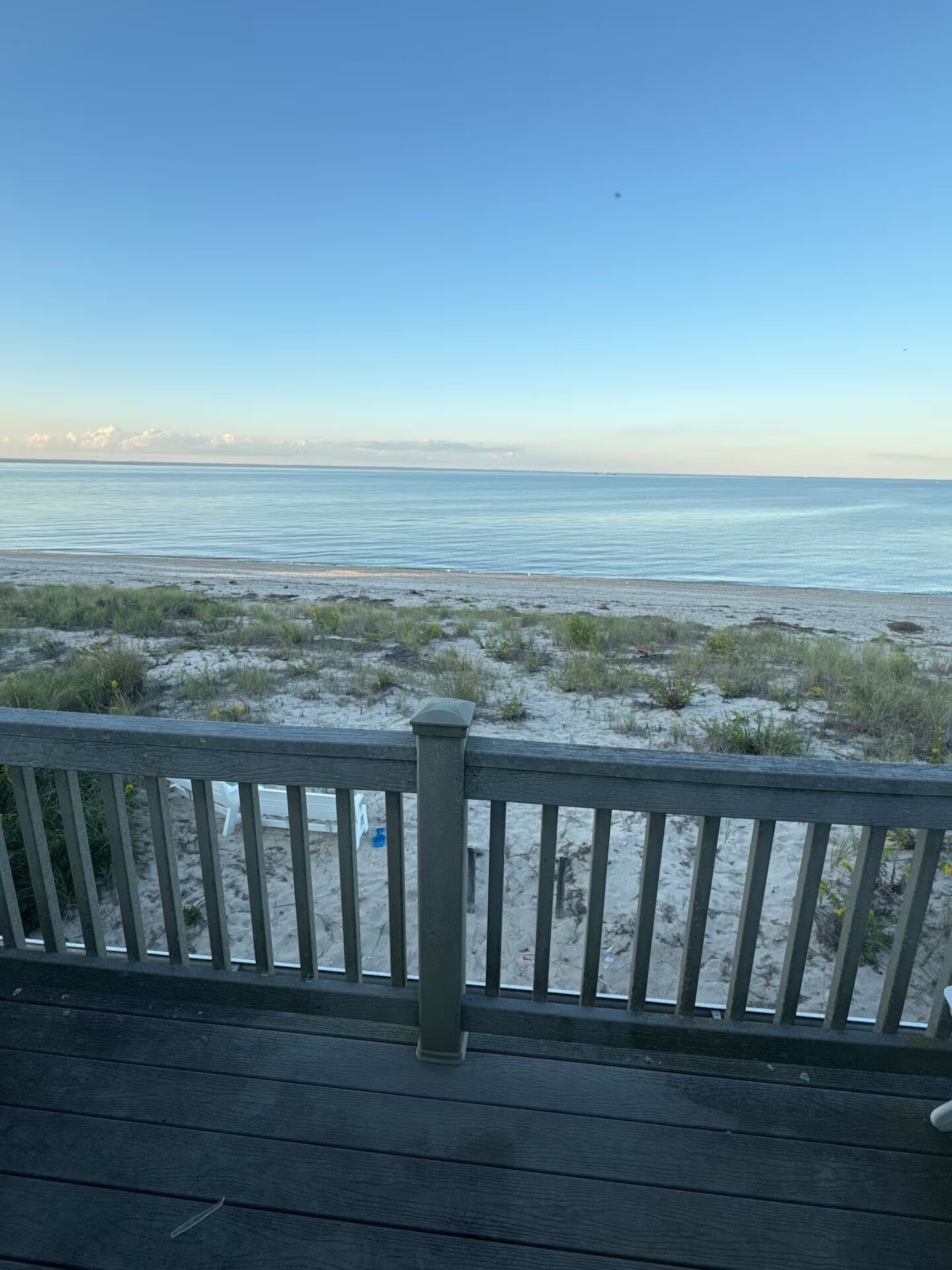 Une terrasse en bois dotée d’une rambarde, qui offre une vue sur une plage de sable où la végétation est clairsemée.