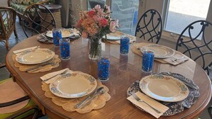 A dining table set with plates, cutlery, and glasses, surrounded by wicker chairs and a view of the beach. - North Shore Breezes Beachfront Home in Asharoken Pet Friendly/Event Friendly (Northport)