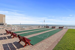 Ein sonniger Außenbereich mit einem Shuffleboard-Spielfeld, Bänken und Blick auf den Ozean.