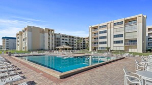 A swimming pool surrounded by lounge chairs and a building with multiple balconies. - Castle Reef 407 (New Smyrna Beach)