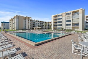 Ein Swimmingpool, umgeben von Liegestühlen und einem Gebäude mit mehreren Balkonen.