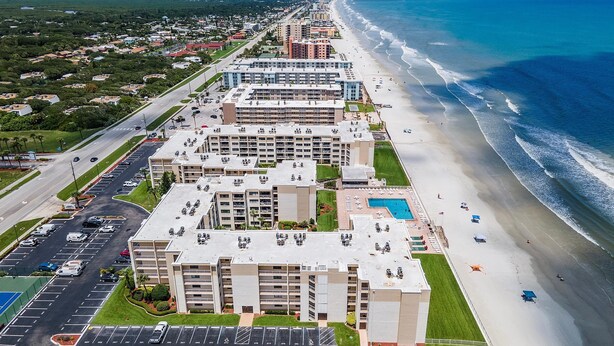 A beachfront hotel with multiple buildings, a parking lot, and a beach. - Castle Reef 407 (New Smyrna Beach)