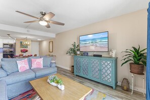 Sala de estar con sofá, televisor, ventilador de techo y vista a la playa.