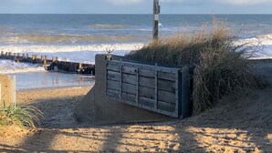 Een strand met een richtingwijzer en een betonbarrière.