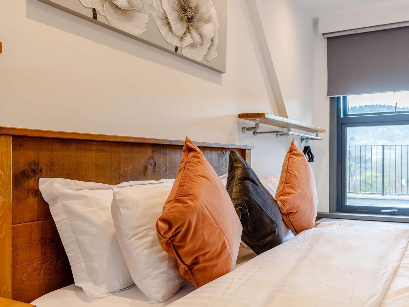 Una cama con almohadas blancas y marrones, un cabecero de madera y vistas al exterior a través de una ventana.