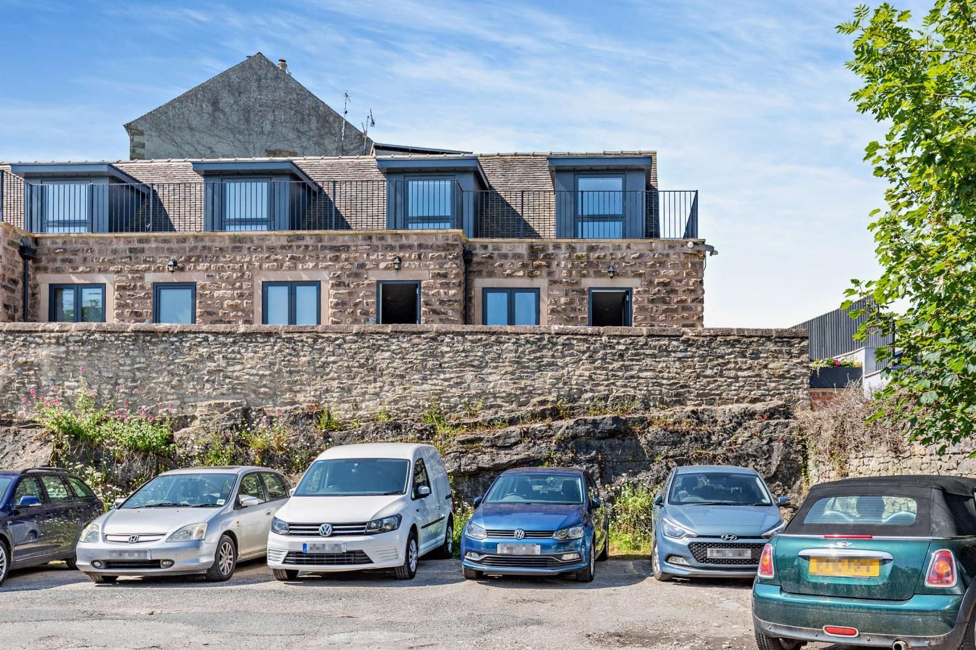 A multi-story building with a stone facade, several windows, and a parking lot with various cars.