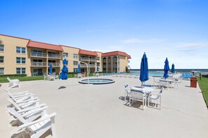 A hotel pool area with lounge chairs and umbrellas, a pool, and a building with balconies. - Point East 205 (New Smyrna Beach)