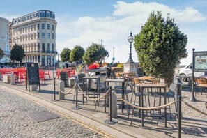 An outdoor cafe area with tables and chairs, a statue, and a historic sign.
