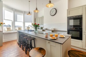 A modern kitchen with a central island, bar stools, a clock, and a view of the city.
