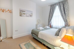 A bedroom with a bed, a bedside table with a lamp, a mirror, a painting on the wall, and a window with curtains. - 5 Bed in Margate (oc-86551) (Margate)