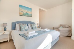 A hotel room with a bed, a chair, a nightstand, and a painting on the wall.