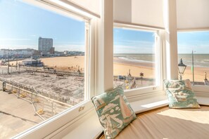 A room with a view of a beach and a pier, featuring a bed with pillows and a window with a view.