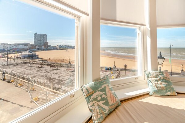 A room with a view of a beach and a pier, featuring a bed with pillows and a window with a view.