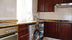 Una cocina con lavadora y secadora integradas, armarios de madera, una campana extractora de acero inoxidable y un salpicadero de azulejos.