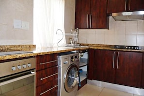 Cozinha com máquina de lavar e secar embutidas, armários de madeira, exaustor de aço inoxidável e painel de azulejos.