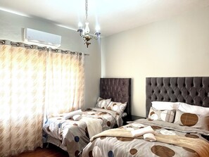 A hotel room with two beds, a chandelier, an air conditioning unit, and a curtain. - Room-luxurious Room - B (Johannesburg)