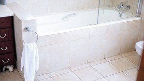 Un baño moderno con una bañera de hidromasaje con mampara de vidrio, un lavamanos blanco y un tocador de madera.