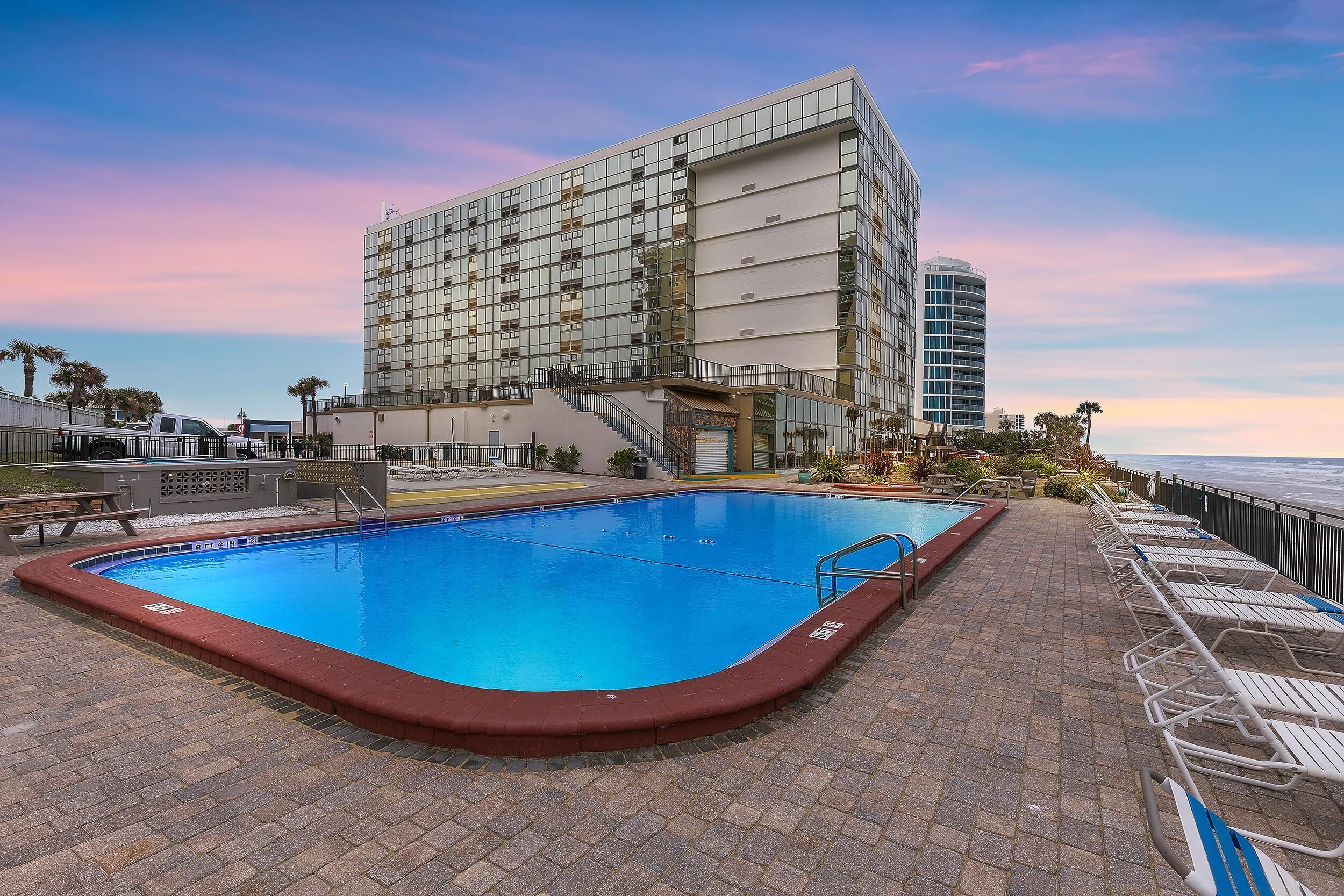 A swimming pool with a red border, lounge chairs, and a building with a glass facade in the background.