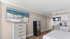 A bedroom with a bed, a dresser, a refrigerator, and a kitchen area with a microwave. - Oceanside Inn 605 (Daytona Beach Shores)
