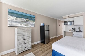 Ein Schlafzimmer mit einem Bett, einem Schminktisch, einem Kühlschrank und einer Küchenzeile mit einer Mikrowelle.