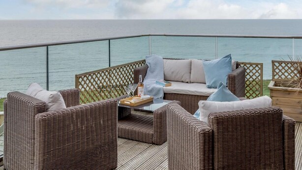 Una terrazza con mobili in vimini, ringhiera in vetro e vista sul mare.