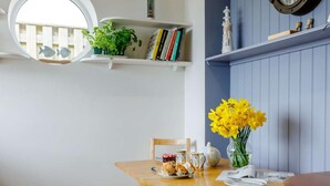 Un'area pranzo con un tavolo in legno, sedie, un vaso di fiori gialli e una libreria con libri e oggetti decorativi.