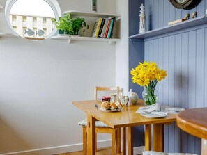 A dining area with a wooden table, chairs, a vase of yellow flowers, and a bookshelf with books and decorative items. - 4 Bed in Bridport (oc-86538) (Bridport)