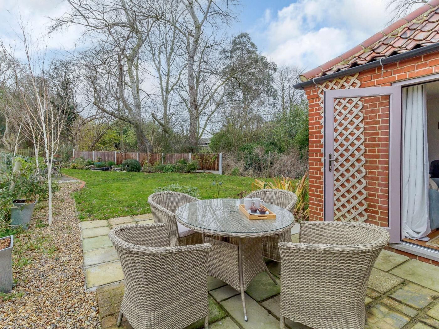 A patio with wicker furniture, a glass table, and a brick wall with a lattice design.