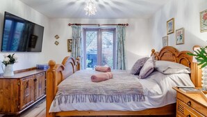 Un dormitorio con una cama de madera, televisor, cómoda de madera y ventana con cortinas.