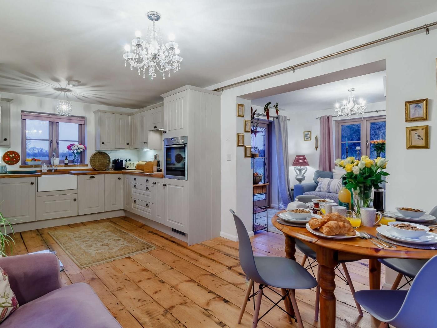 A modern kitchen with white cabinets, a dining area with a wooden table, and a chandelier.