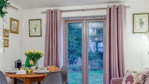 Un comedor con una mesa lista para el desayuno, un sofá y un ventanal corredero que da a un jardín.