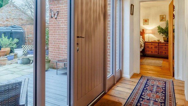 Una habitación con una puerta corrediza de vidrio que da a un patio, suelo de madera, alfombra estampada y pared de ladrillo.