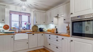 Una cocina con armarios blancos, encimera de madera, horno empotrado y ventana con vistas.