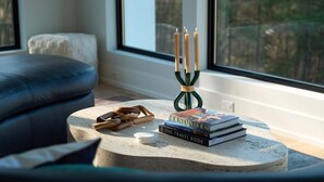 Una mesa redonda con una pila de libros, un candelabro y un pequeño objeto de madera.