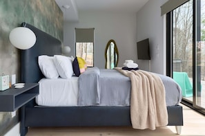 Un dormitorio moderno con una cama grande, mesitas de noche, un televisor montado en la pared y un ventanal con vistas.
