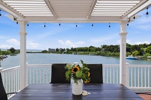 Un espacio de estar al aire libre cubierto con vistas a un cuerpo de agua, una mesa con un jarrón de flores y una silla.