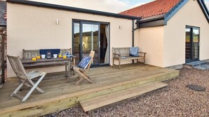 A building with a wooden deck, a bench, a table with breakfast items, and a sliding glass door. - 2 Bed in Mindrum (oc-86637) (Carham)