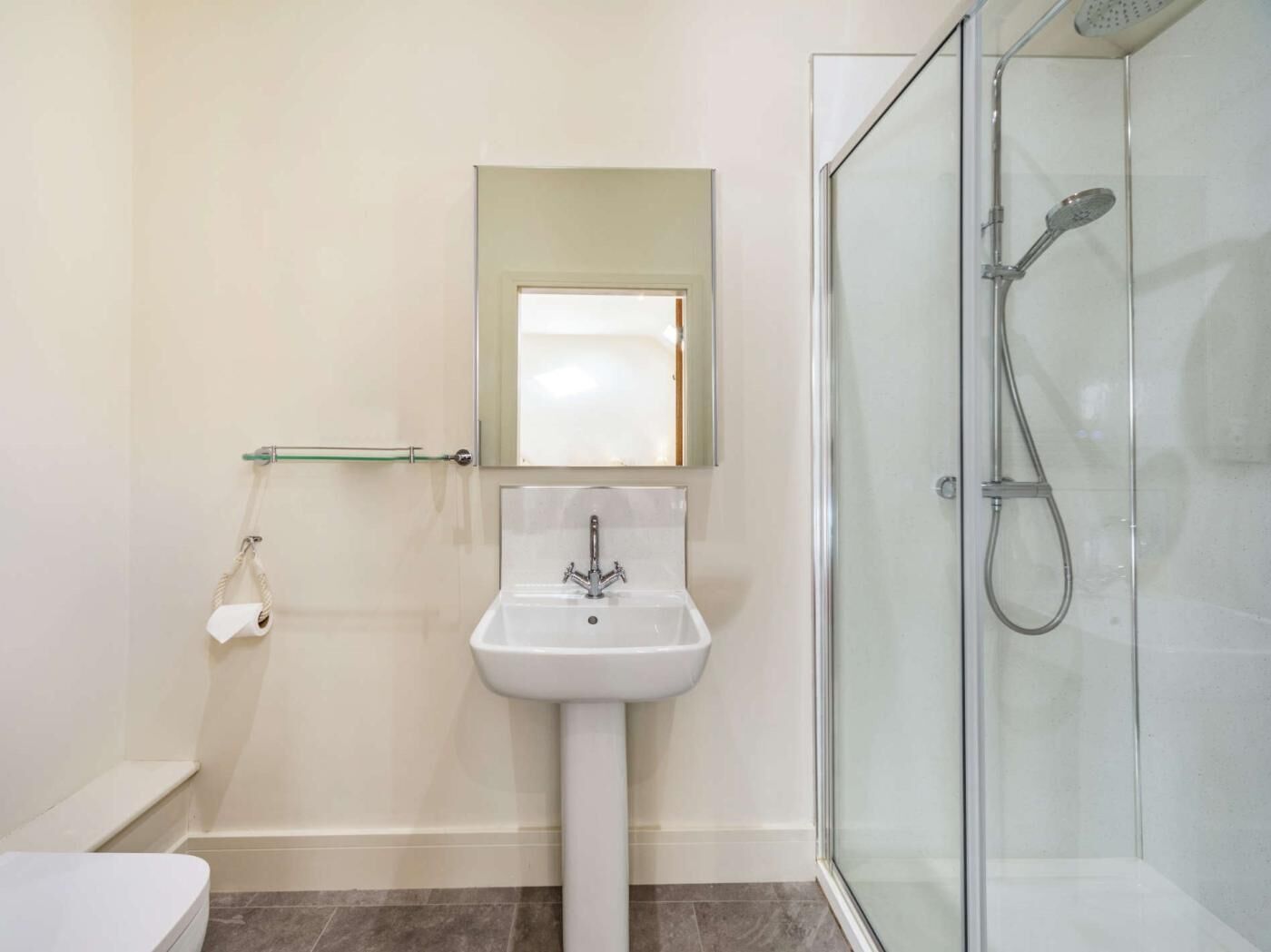 Une salle de bain avec une douche à parois de verre, un lavabo sur colonne et un miroir au-dessus du lavabo.