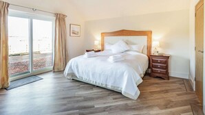 A hotel room with a bed, a nightstand, a wooden headboard, a window with curtains, and a door. - 2 Bed in Mindrum (oc-86637) (Carham)